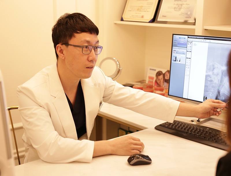 원장이 상담 데스크에서 모니터에 띄운 방사선 영상을 손으로 가리키며 설명하는 장면