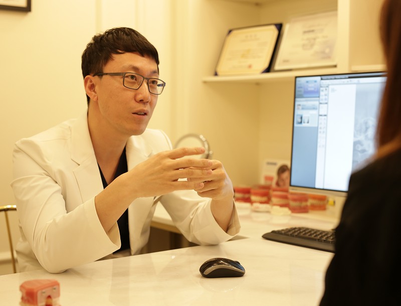 강남에버스마일치과 상담실에서 심형보 대표원장이 상담 테이블에 앉아 환자에게 설명하는 모습